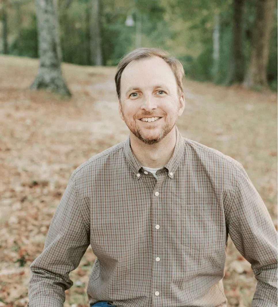 Daniel Richardson smiling outdoors in a wooded setting